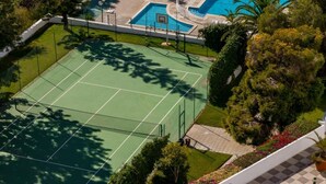 Ilmakuva tenniskentästä, jonka ympärillä on vehreää kasvillisuutta ja sen vieressä uima-allas.