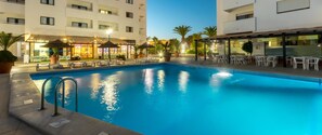 A swimming pool with lounge chairs and umbrellas, surrounded by buildings with outdoor seating and a restaurant. - Apartamentos Turísticos Janelas do Mar (Albufeira)