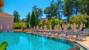 A swimming pool with lounge chairs and umbrellas, surrounded by trees and a building. - Hotel Pine Valley (Fethiye)