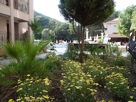Área da piscina com um jardim de flores amarelas, uma árvore e um edifício com varandas.
