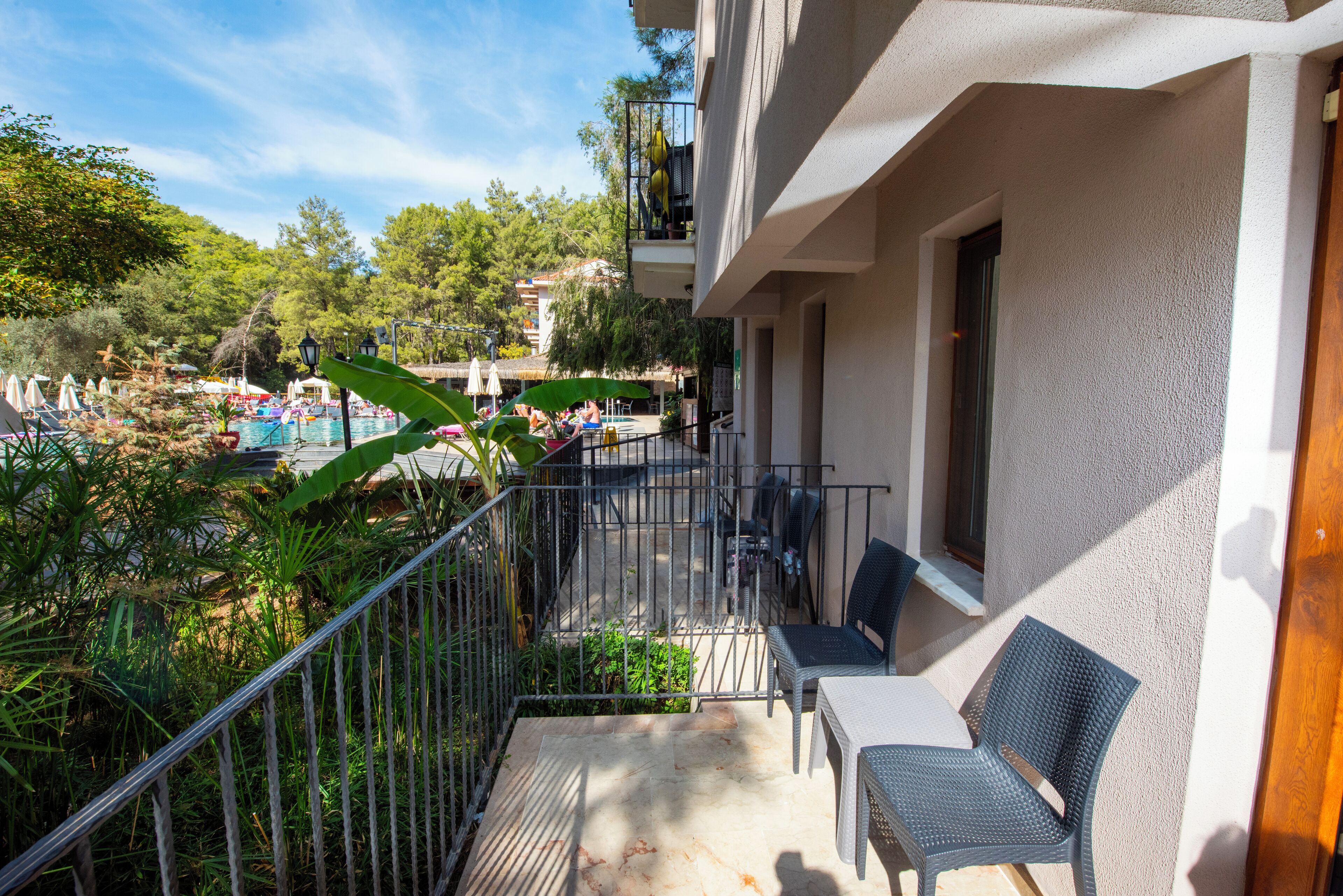 Un balcón con vista a una zona de piscina, mobiliario exterior y abundante vegetación.