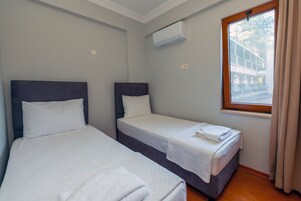 Habitación de hotel con dos camas individuales, una ventana con cortinas, un equipo de aire acondicionado y vistas a un edificio.