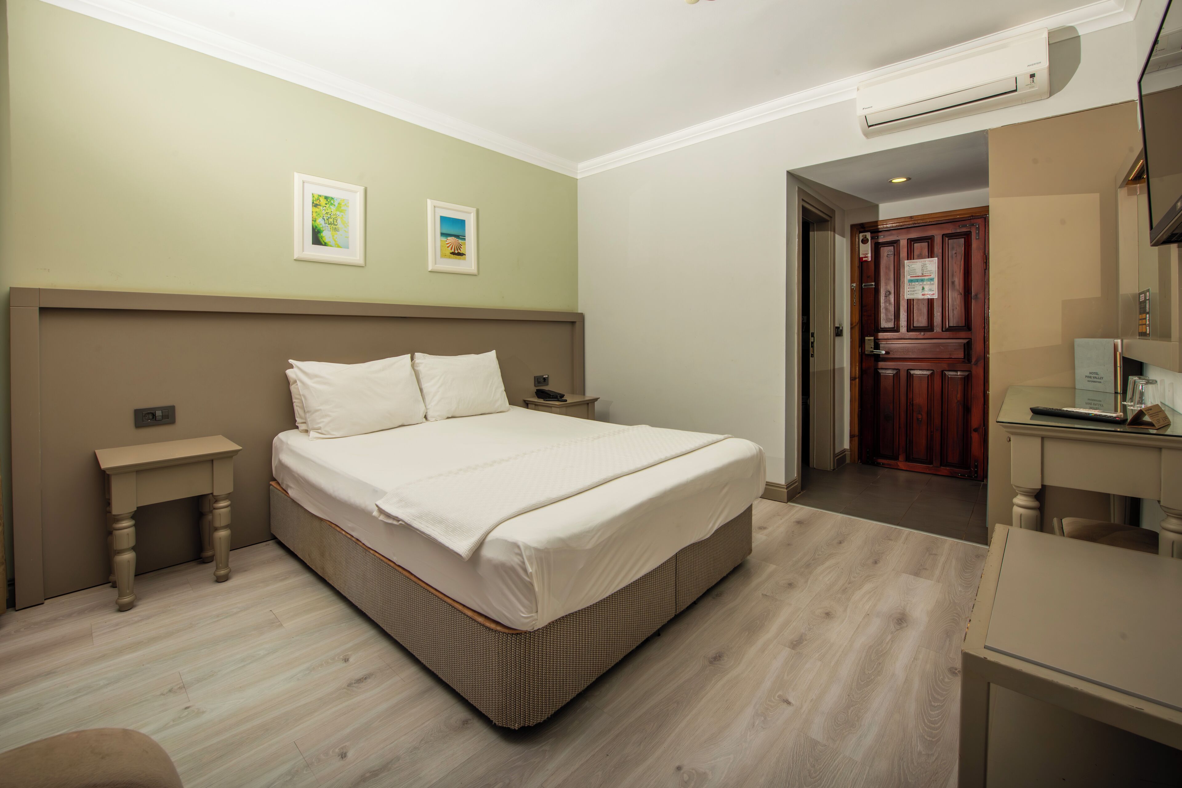 A bedroom with a large bed, bedside tables, a wooden door, and a desk with a chair.