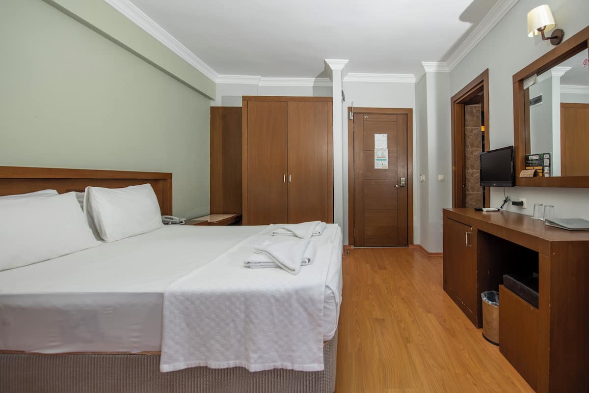 Habitación de hotel con una cama grande, un armario de madera, un escritorio con espejo y una televisión.