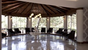 Un espace extérieur aménagé, abrité et doté d’une fontaine centrale, entouré de chaises et de tables, et de grandes fenêtres offrant une vue sur les arbres.