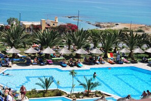 A swimming pool surrounded by palm trees and lounge chairs, with a view of the sea. - Mediterraneo Hotel - All Inclusive (Hersonissos)