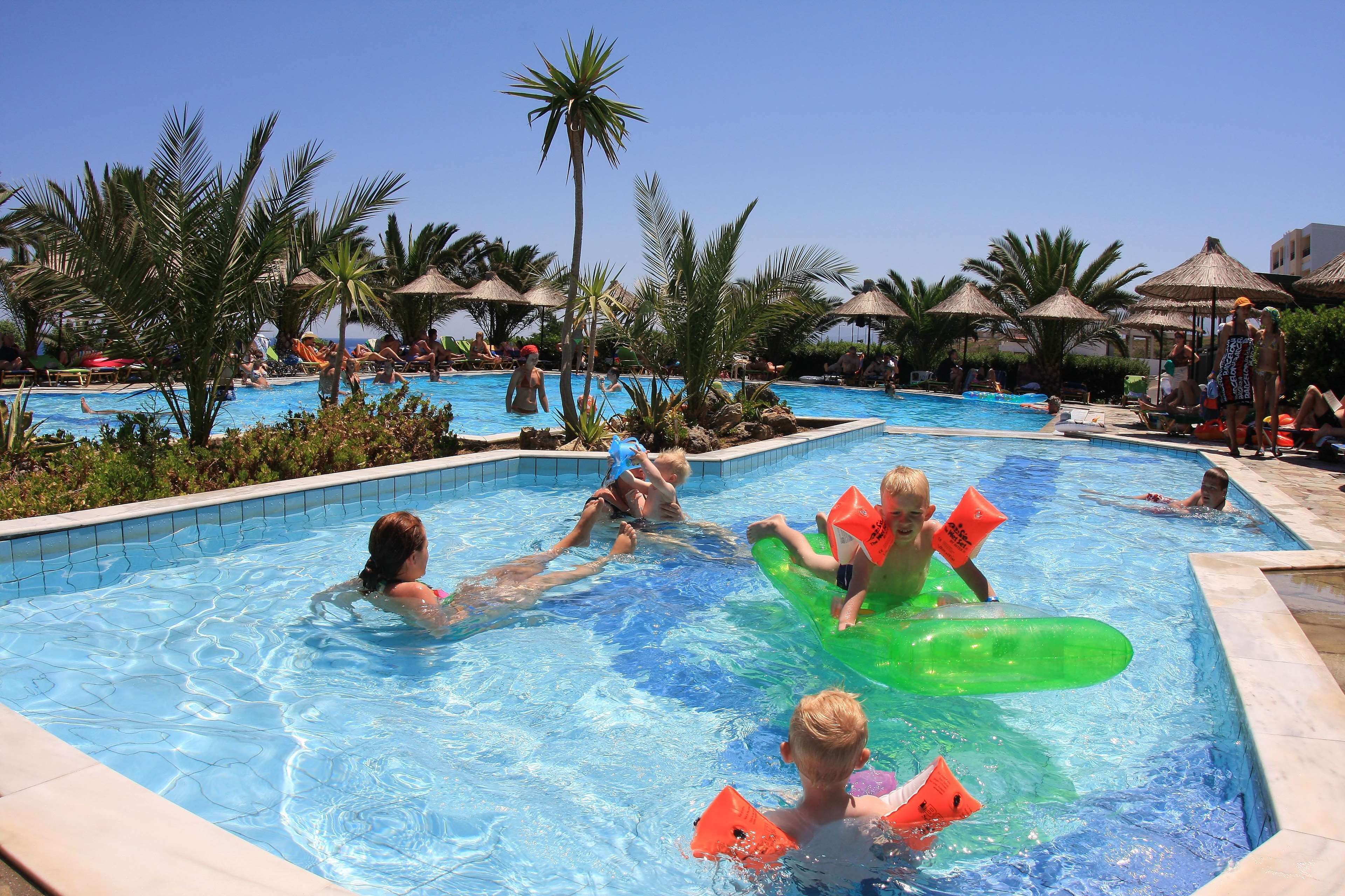 A swimming pool area with multiple pools, palm trees, and lounge chairs.