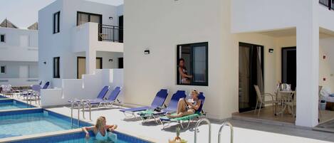 A pool area with lounge chairs and a person swimming.