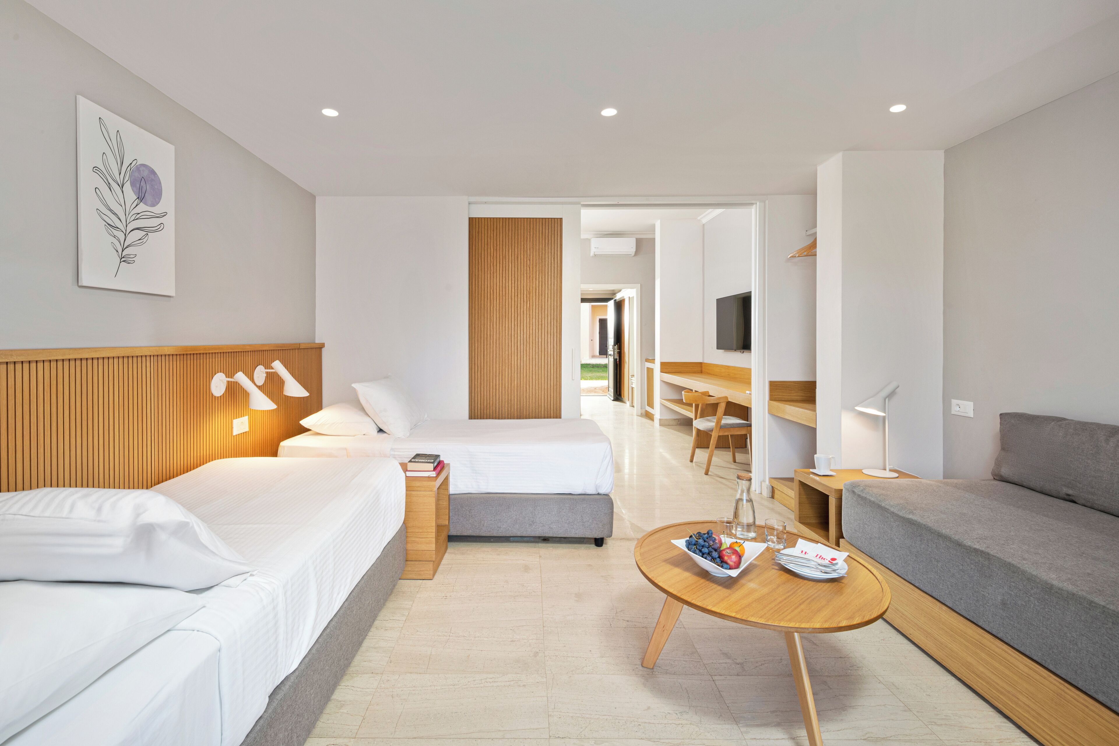 A modern hotel room with a bed, a sofa, a dining area, and a TV.