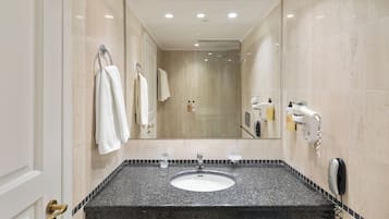 Ein modernes Badezimmer mit einer Granittheke, einem Waschbecken und einem Spiegel. Handtücher hängen an der Wand und ein Föhn ist dort angebracht.