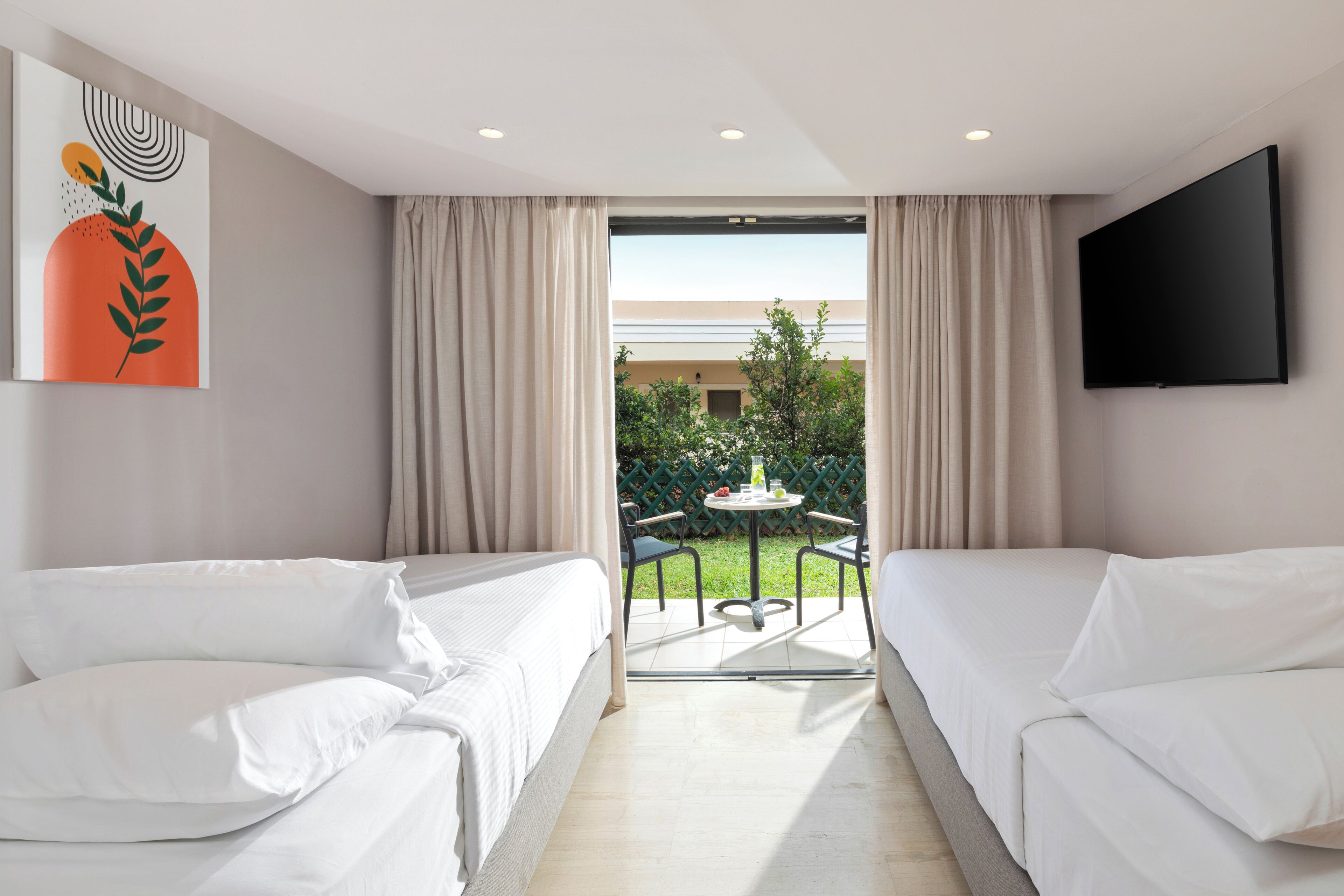 A hotel room with two beds, a TV, and a view of a garden and building outside.