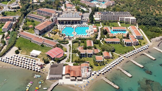 An aerial view of a resort with multiple swimming pools, a beach area with umbrellas, and a pier extending into the water. - Roda Beach Resort & Spa All-inclusive (Corfu)