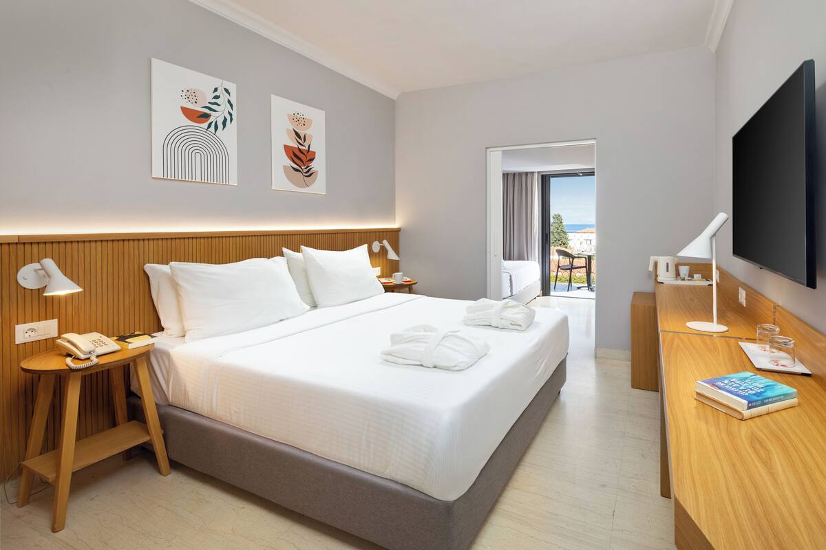 Una camera d'albergo con un letto, comodini, televisione e opere d'arte alle pareti.
