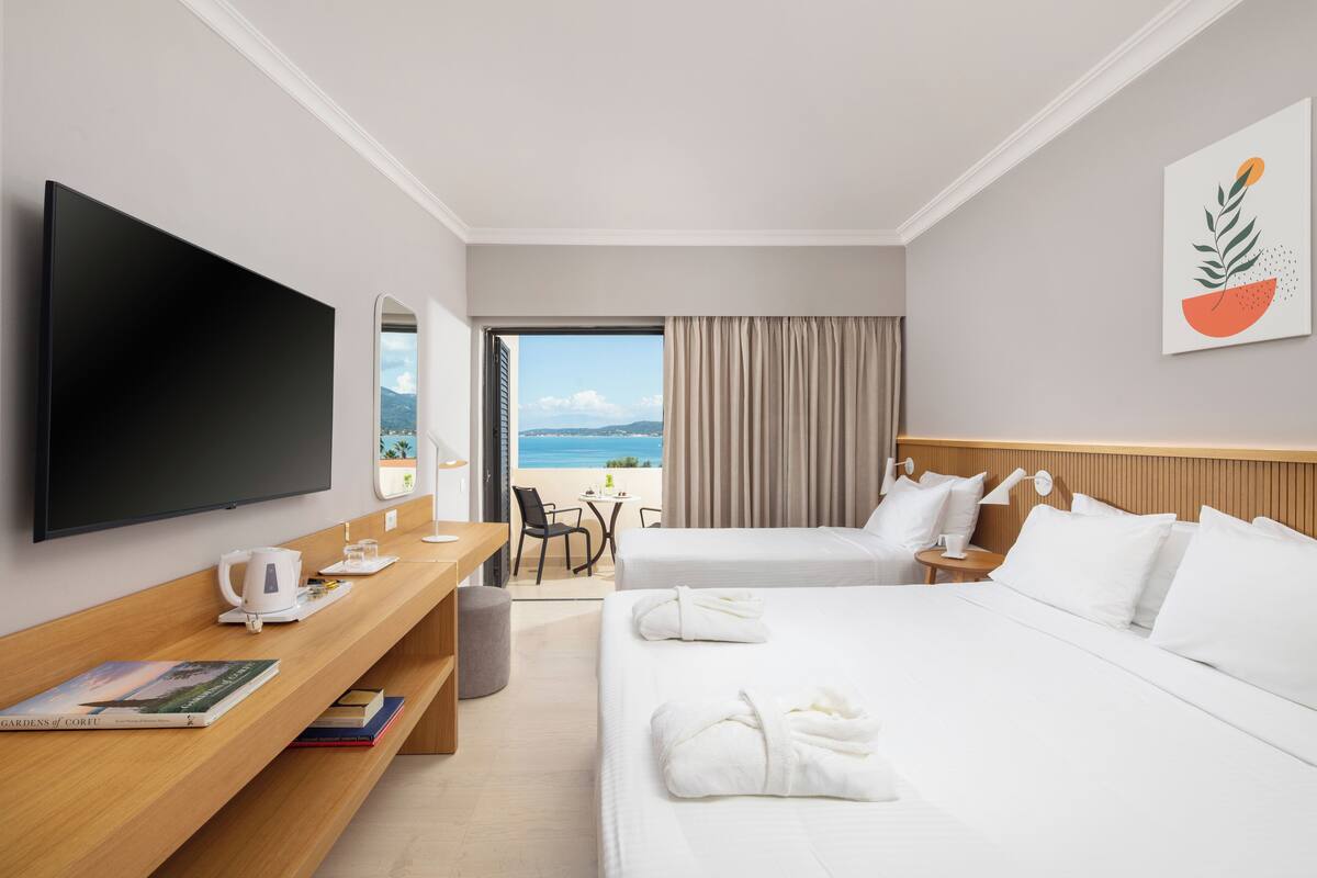 Camera d'albergo con due letti, televisione, scrivania con macchina del caffè e vista sulla spiaggia.