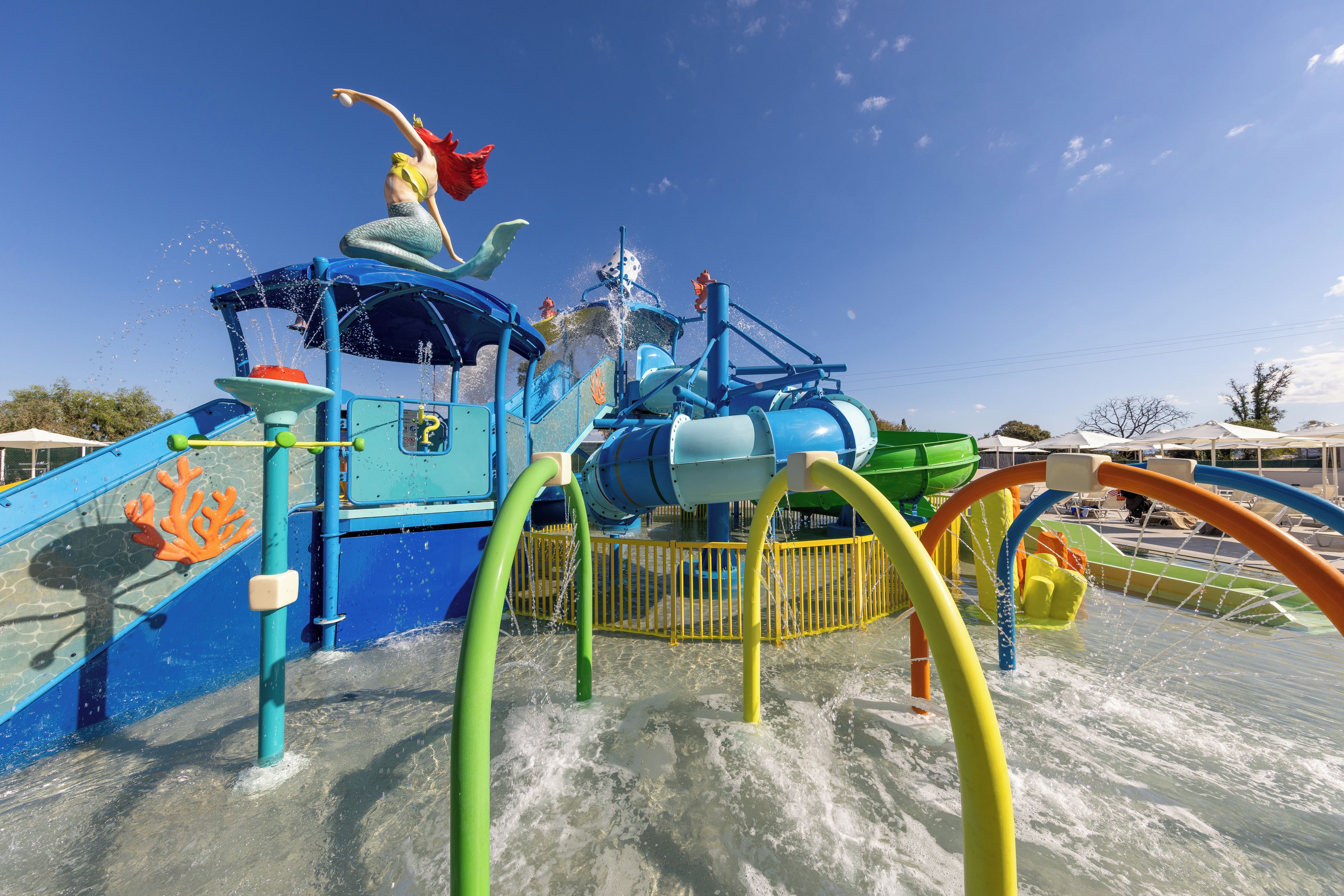 A water park with a water slide, splash pad, and a mermaid statue.