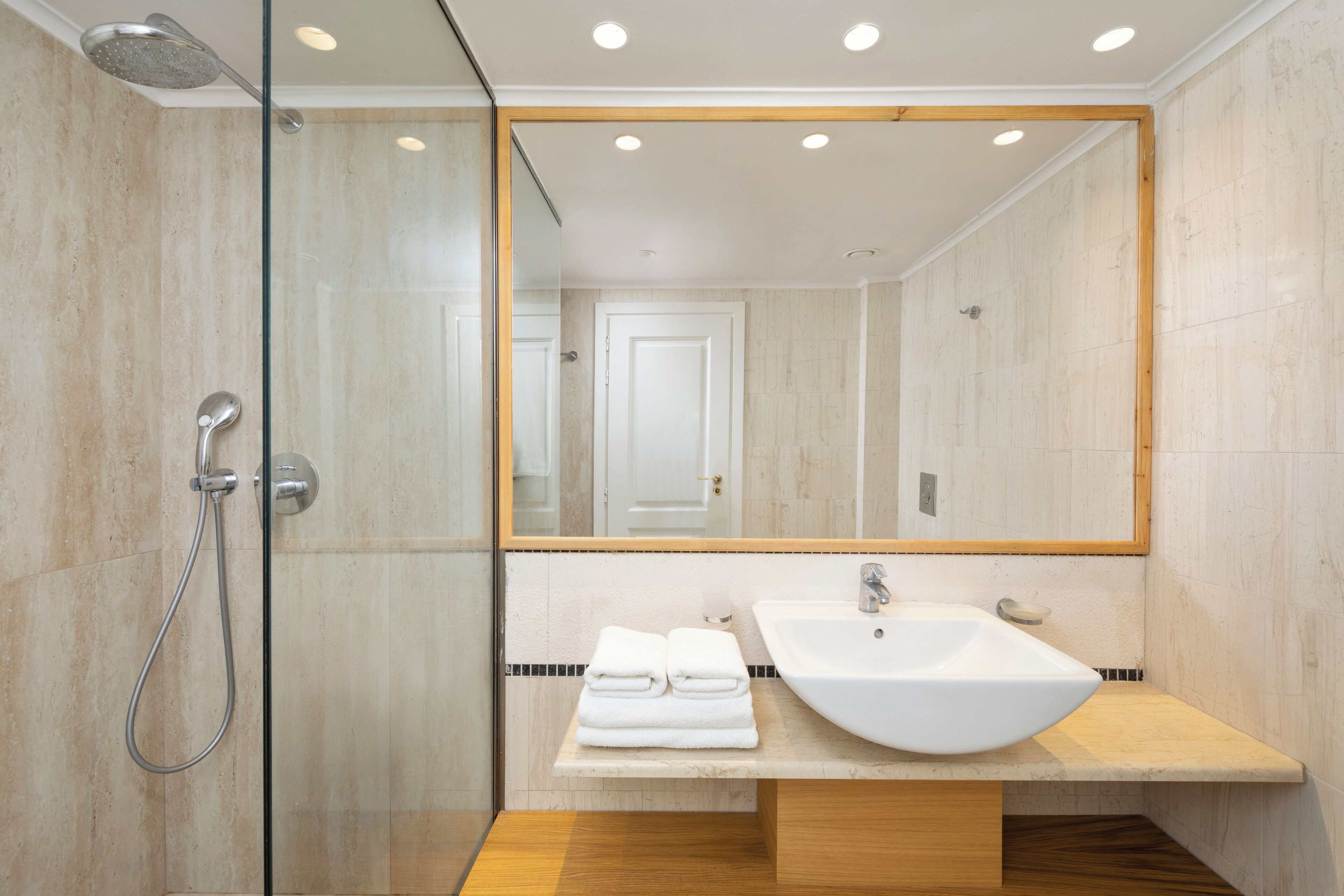 A modern bathroom with a glass-enclosed shower, a large mirror, and a sink with a wooden countertop.