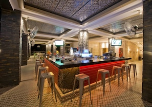 Uma área de bar com banquetas, balcão e teto estampado.