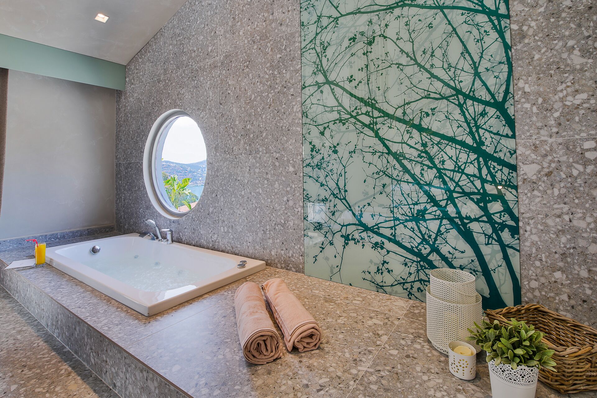 A bathroom with a large bathtub, a round window, and a wall mural.