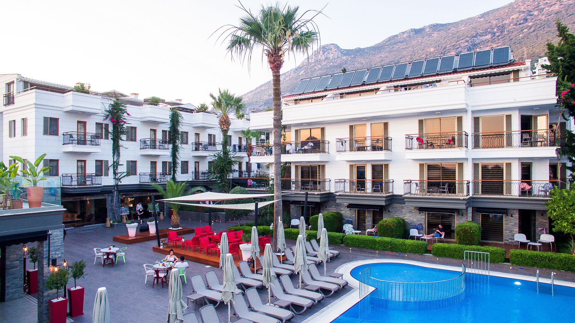 A hotel courtyard with a swimming pool, outdoor seating, and multiple balconies.
