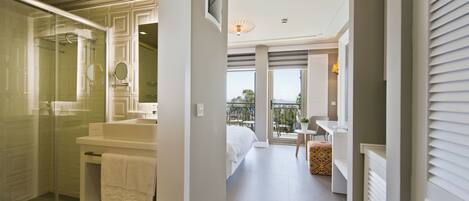 Une chambre d’hôtel moderne dotée d’une douche en verre, d’un grand lit, d’un balcon avec vue et d’une petite table avec une chaise.