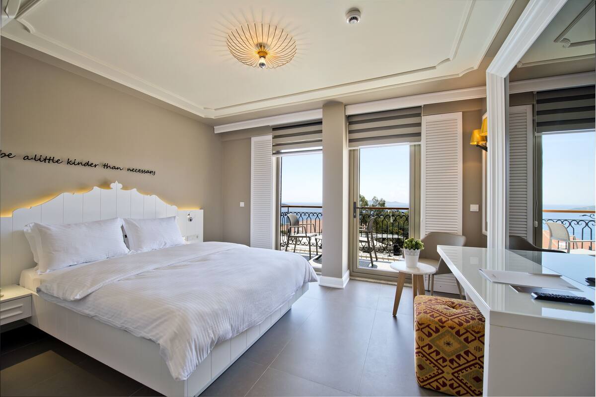A bedroom with a large bed, a desk, and a balcony with a view.
