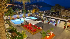 A rooftop pool area with multiple seating areas, a bar, and a view of the city at night. - Samira Exclusive Hotel & Apartments (Kas)