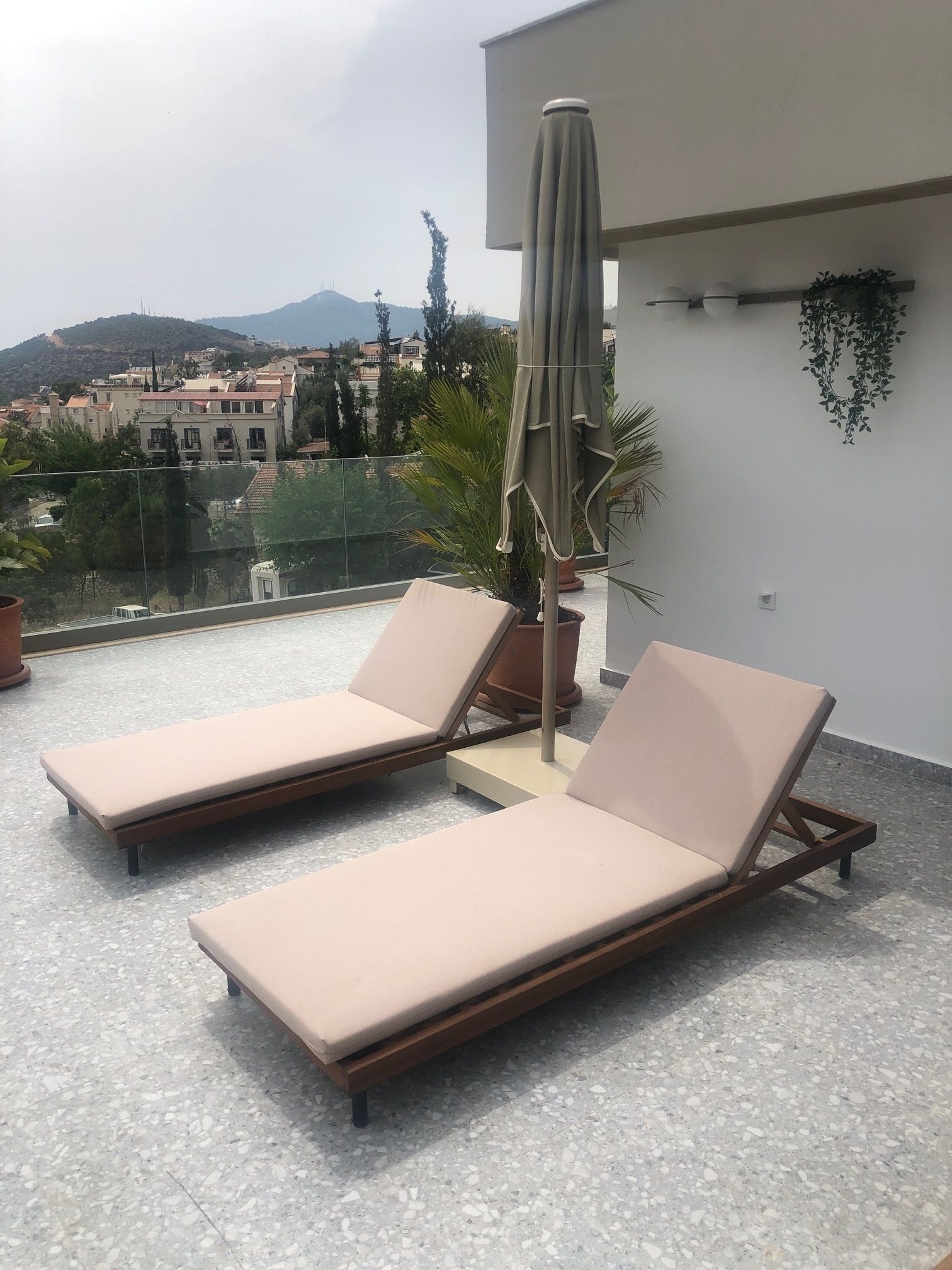 A rooftop terrace with two lounge chairs and a table, a potted plant, and a hanging plant.