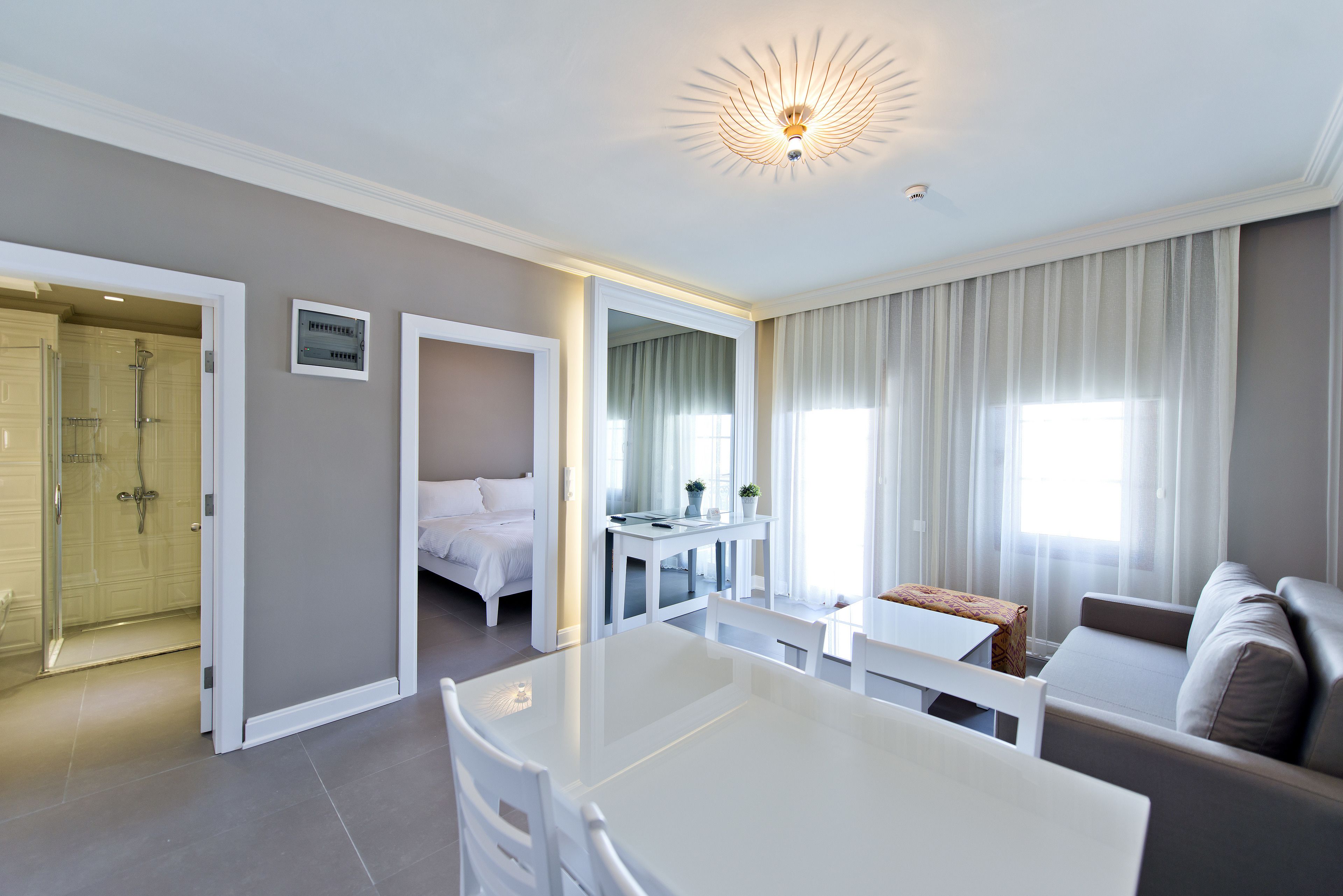 A modern hotel room with a white bed, a dining table, a sofa, and a shower area.