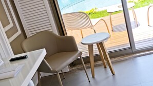 A modern room with a sofa, a small table, and a chair near a sliding glass door leading to an outdoor area with a pool. - Samira Exclusive Hotel & Apartments (Kas)
