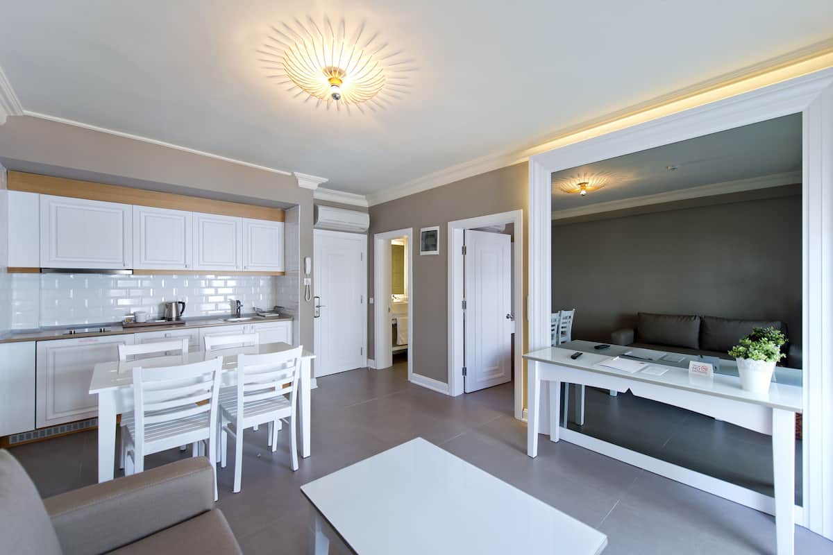 A modern kitchen with white cabinets, a dining area with a white table and chairs, and a living area with a sofa and a coffee table.