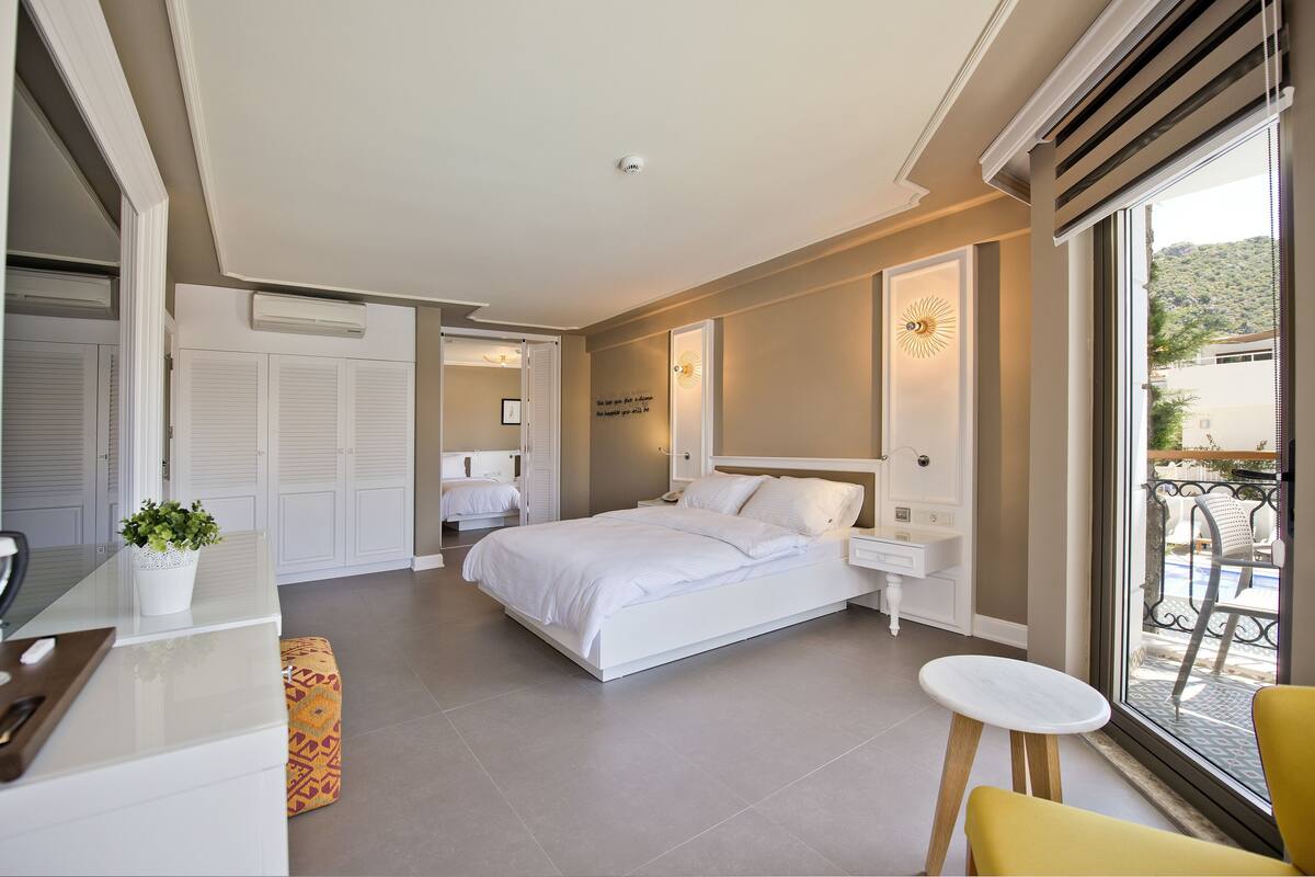 A bedroom with a bed, bedside tables, a small table, a chair, and a window with a view of the outside.