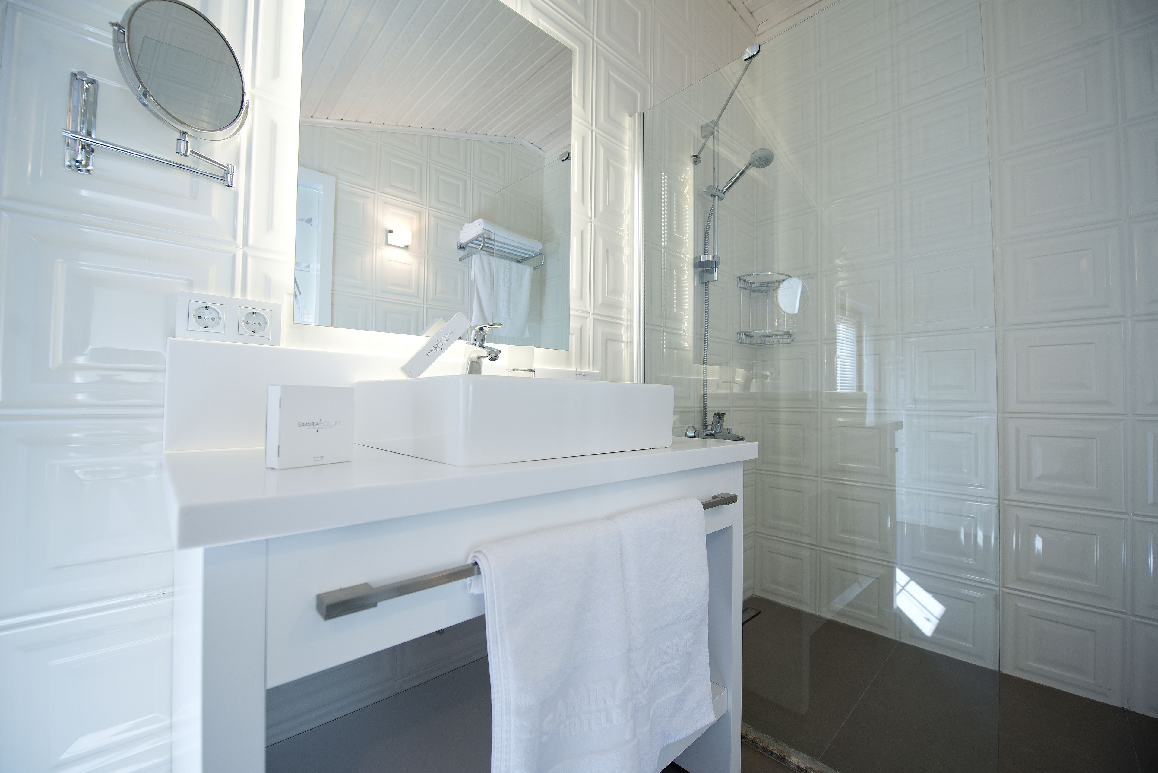 A modern bathroom with a white vanity, a large mirror, a shower enclosure, and a towel rack.