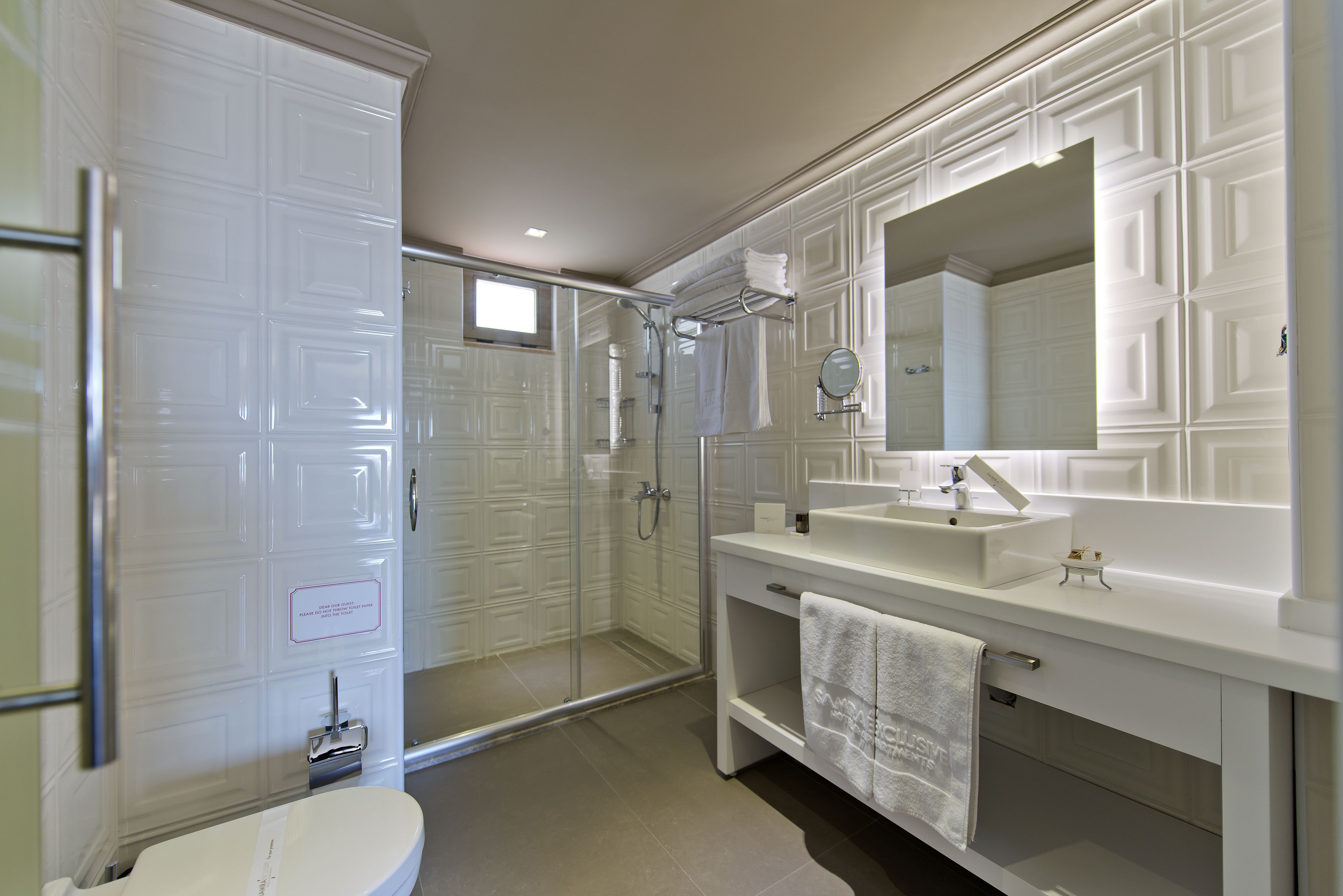 Un baño moderno con cabina de ducha de vidrio, un lavamanos blanco y un espejo grande.