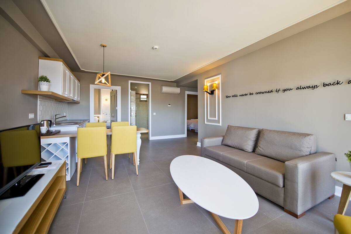 A modern living room with a sofa, a dining table with chairs, and a kitchen area with cabinets and a countertop.