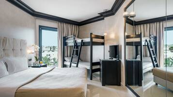 A hotel room with a large bed, a desk, two bunk beds, a TV, and a view of the city.
