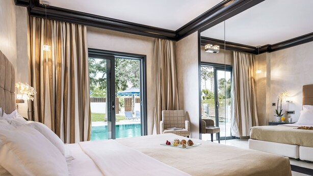 Amplia habitación de hotel con una cama grande, otra cama adicional, zona de estar y vistas a una piscina.