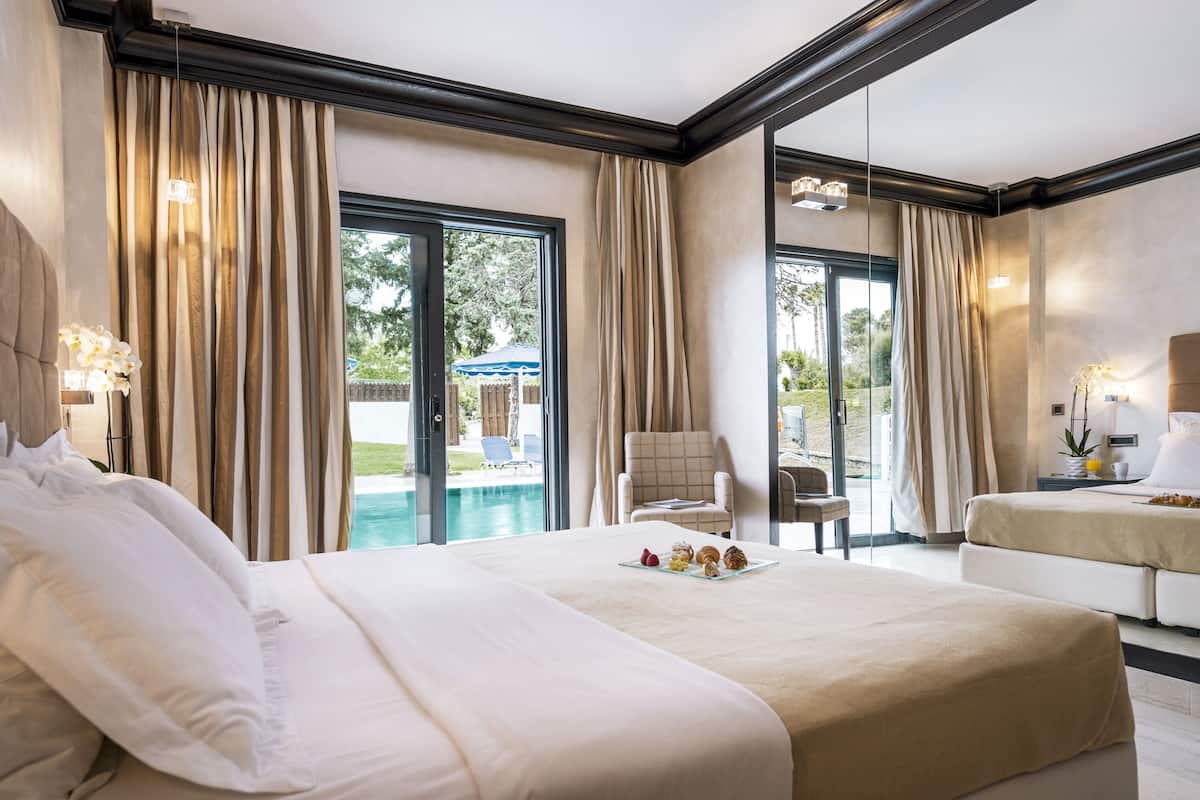 A spacious hotel room with a large bed, a second bed, a seating area, and a view of a swimming pool.