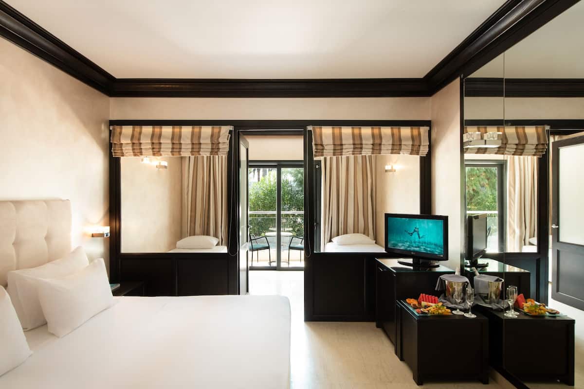 A hotel room with a bed, a TV, a small table with food and drinks, and a balcony with curtains.