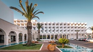 Un hotel con piscina, palmeras y un edificio blanco con balcones.