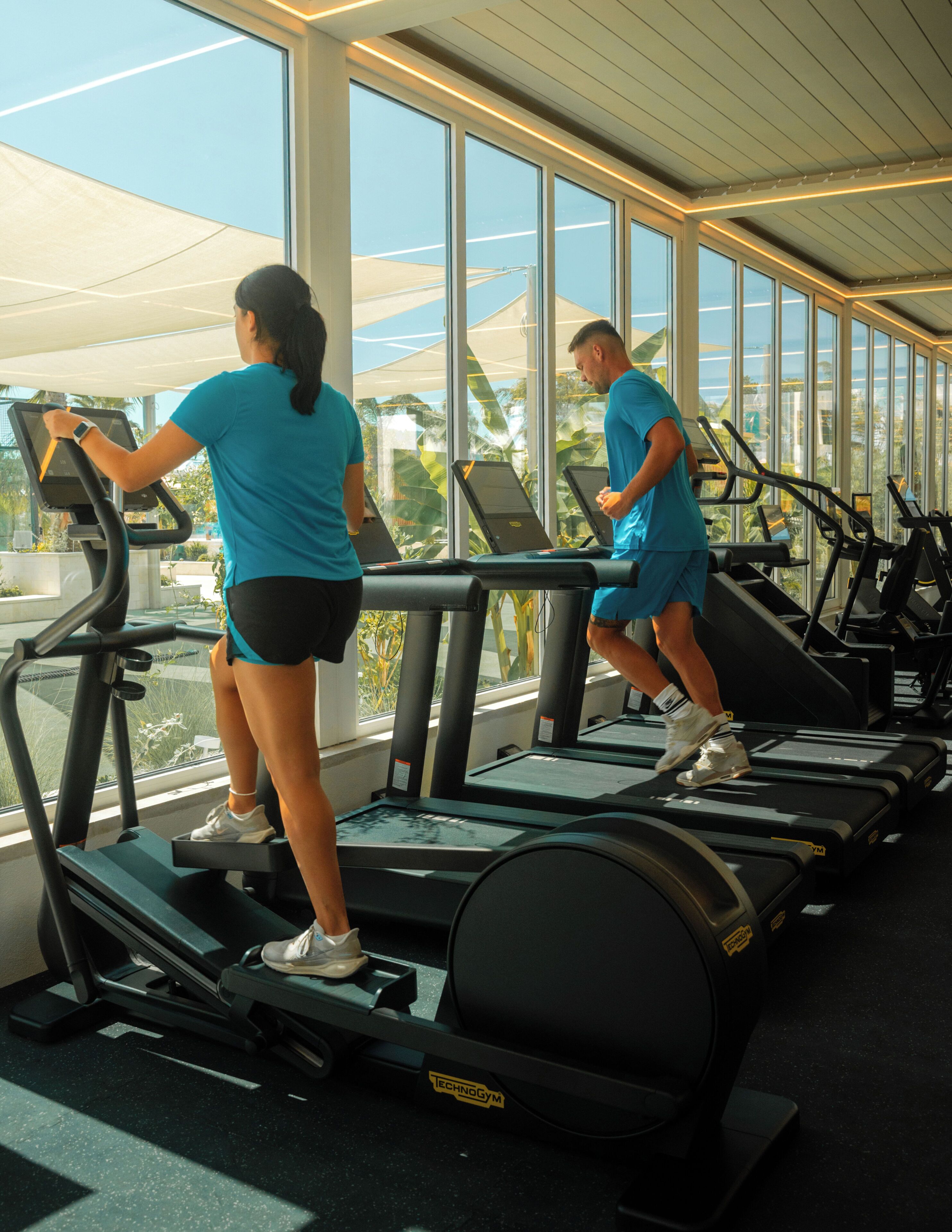 Un gimnasio con cintas de correr y equipo de ejercicio, amplias ventanas y vistas al exterior.