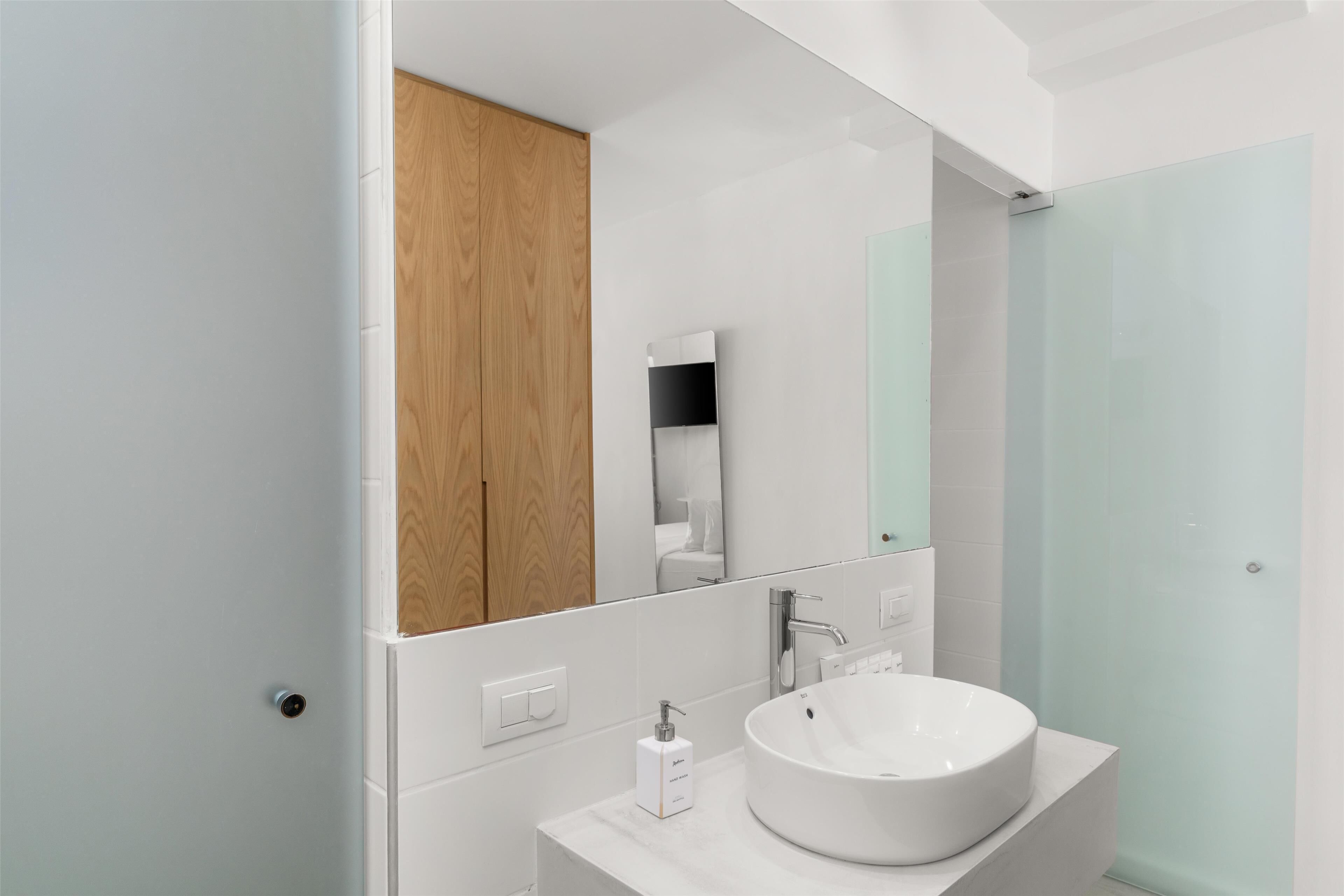 A modern bathroom with a white sink, a wooden cabinet, and a glass shower enclosure.