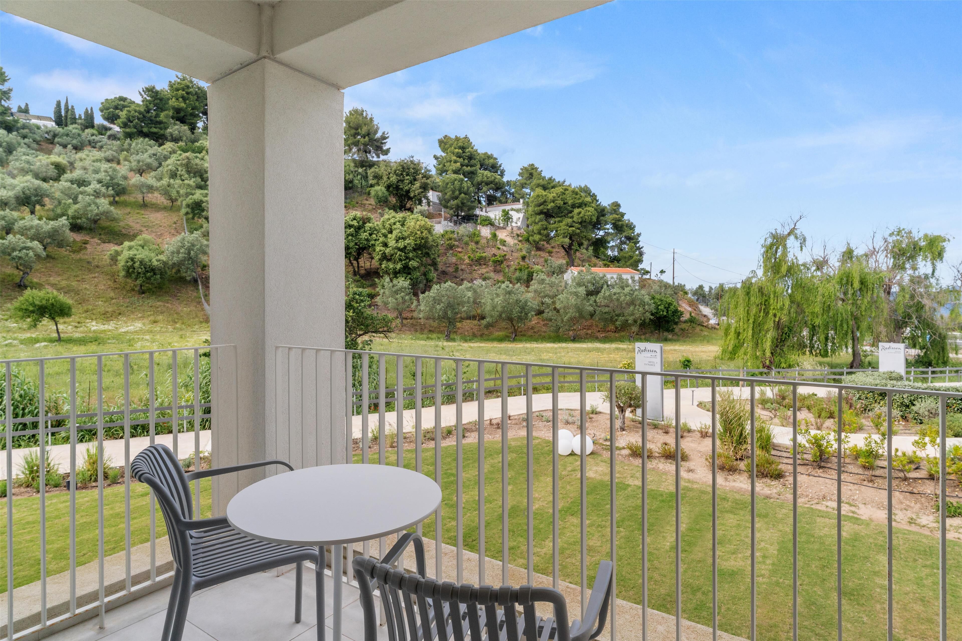 Ein Balkon mit Tisch und Stühlen, der auf einen angelegten Garten mit verschiedenen Pflanzen und Bäumen blickt.