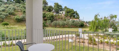 Ein Balkon mit Tisch und Stühlen, der auf einen angelegten Garten mit verschiedenen Pflanzen und Bäumen blickt.