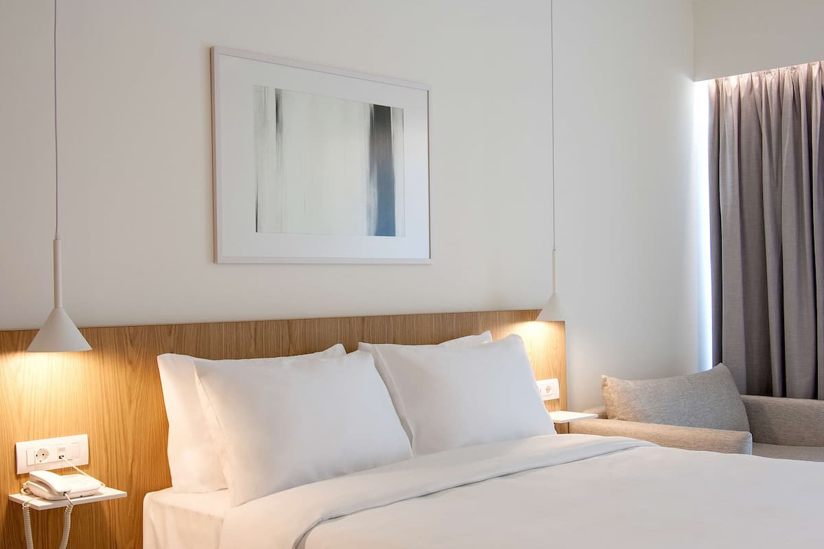 A hotel room with a bed, bedside table, lamp, and a framed picture on the wall.