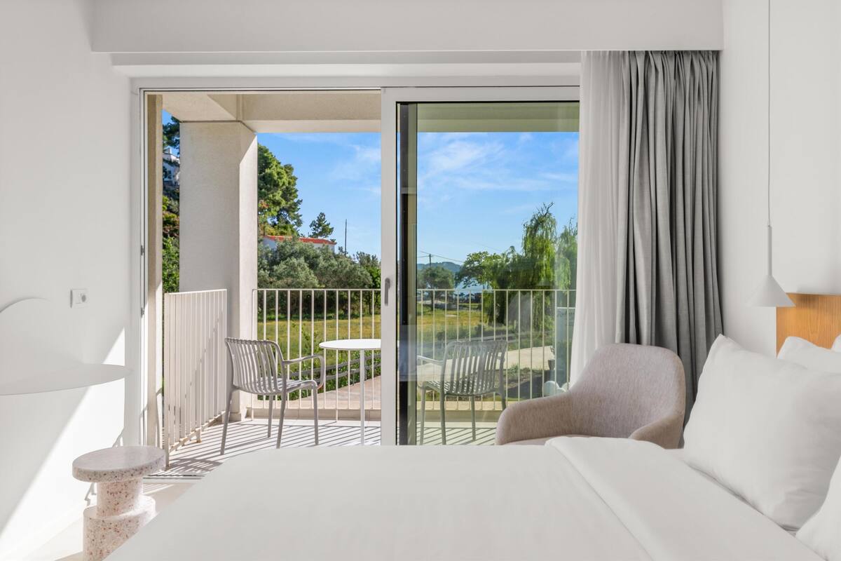 A modern hotel room with a balcony, a bed, a chair, and a table.