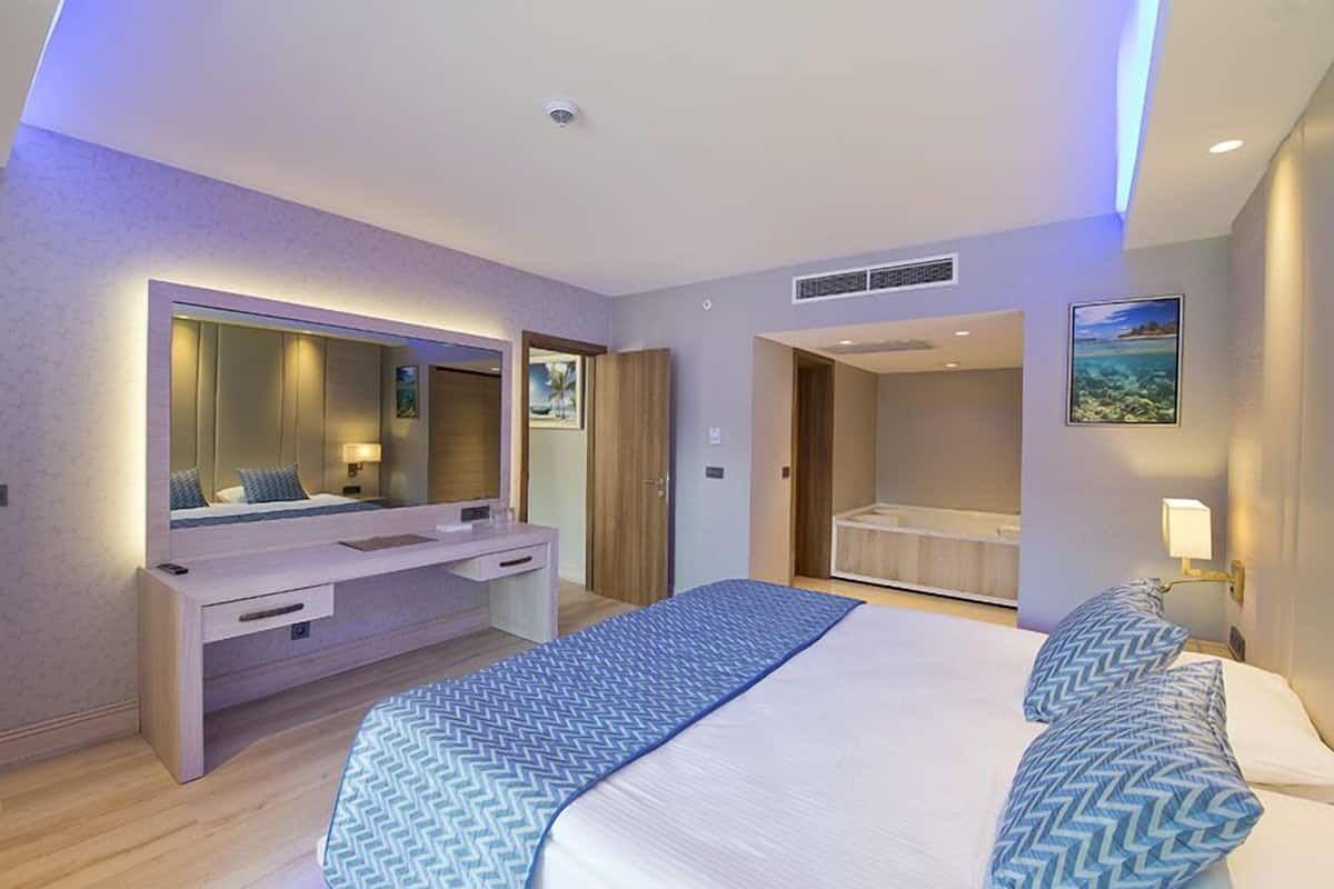 A modern hotel room with a large bed, a desk, and a walk-in closet.