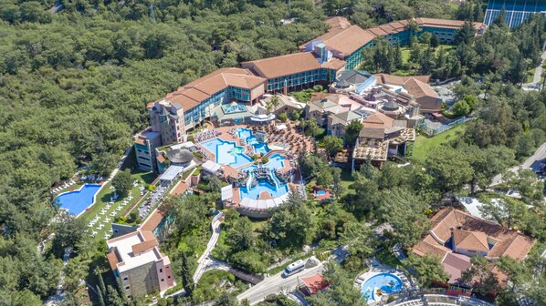 An aerial view of a resort with multiple buildings, a large central pool area, and surrounding greenery.