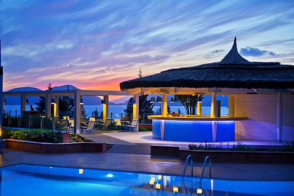 A poolside area with a bar and lounge chairs, overlooking a body of water and mountains.