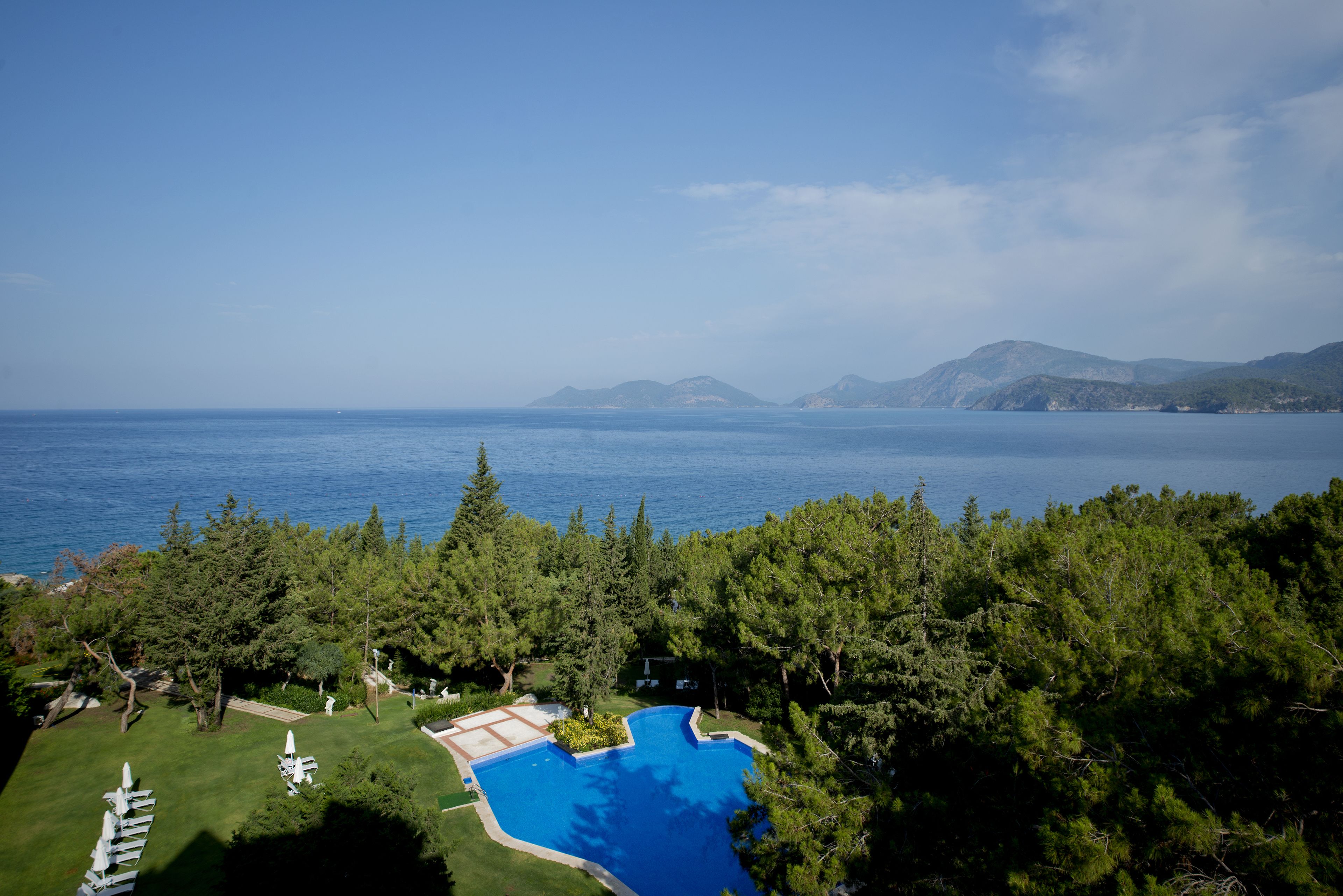 Una piscina rodeada de abundante vegetación y vistas al mar y a las montañas.