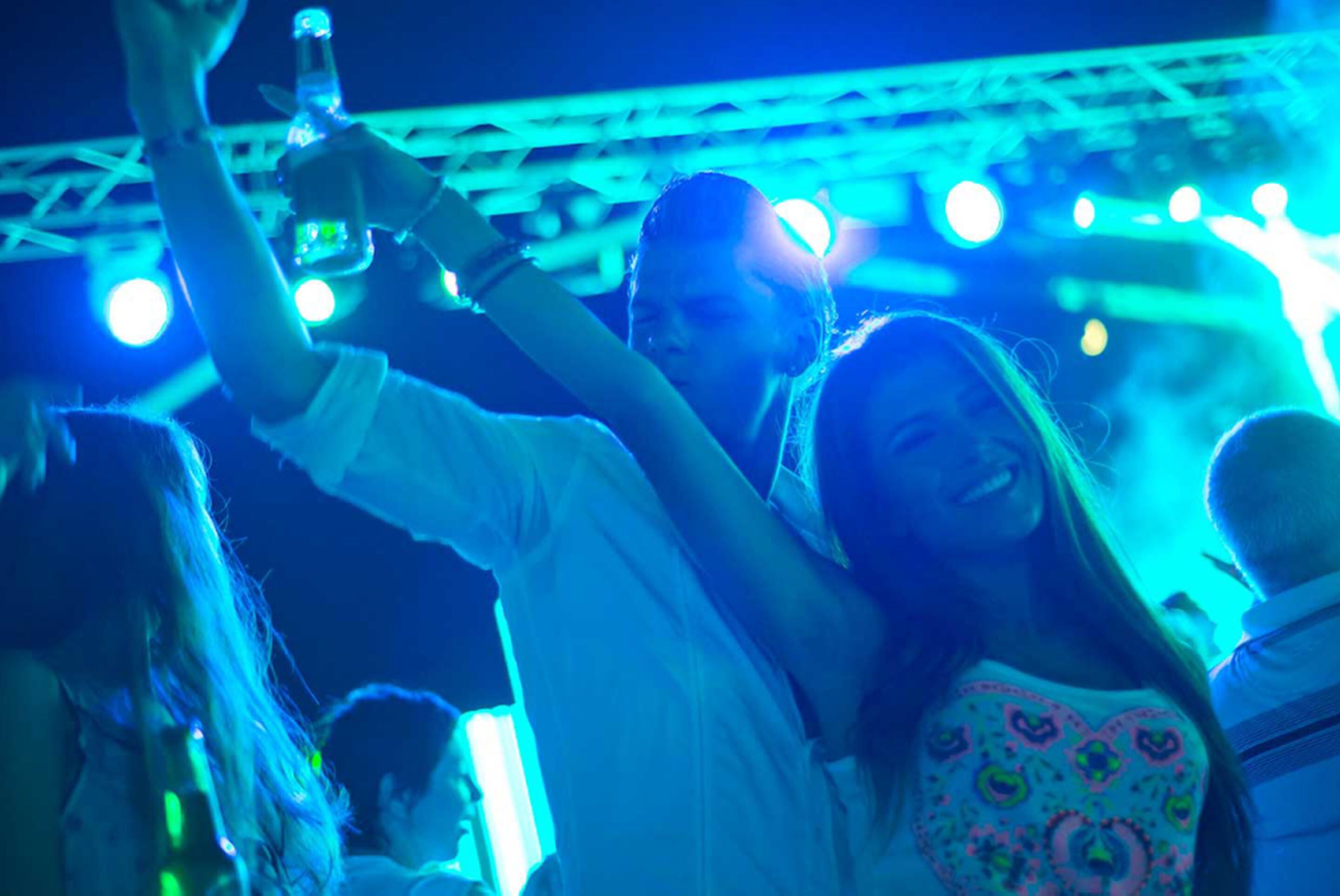 A crowded indoor event with people holding drinks and raising their hands, possibly at a concert or party.